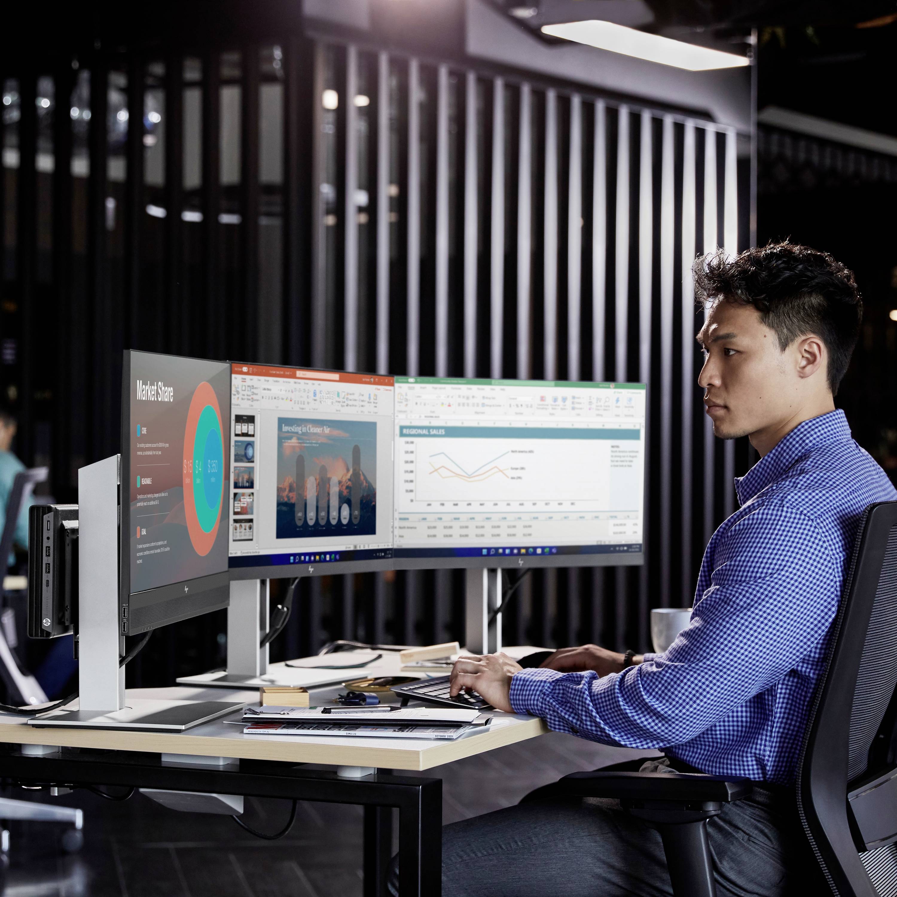 Un homme travaille sur deux écrans dans un bureau moderne. Des diagrammes et des tableaux montrant des analyses de données sont visibles sur les écrans.