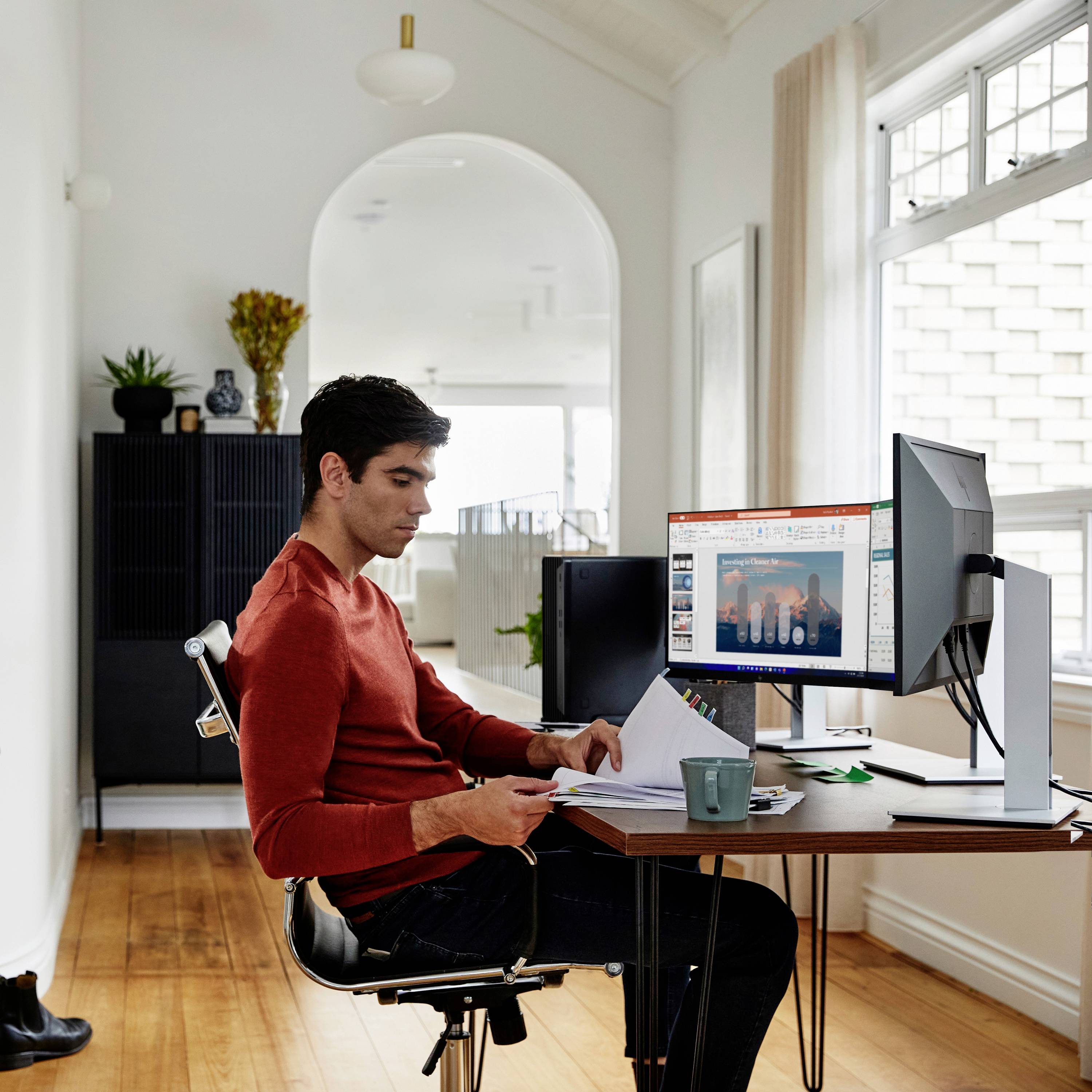 Une personne est assise à un bureau dans un espace de vie et travaille sur un ordinateur. L'écran affiche un graphique.