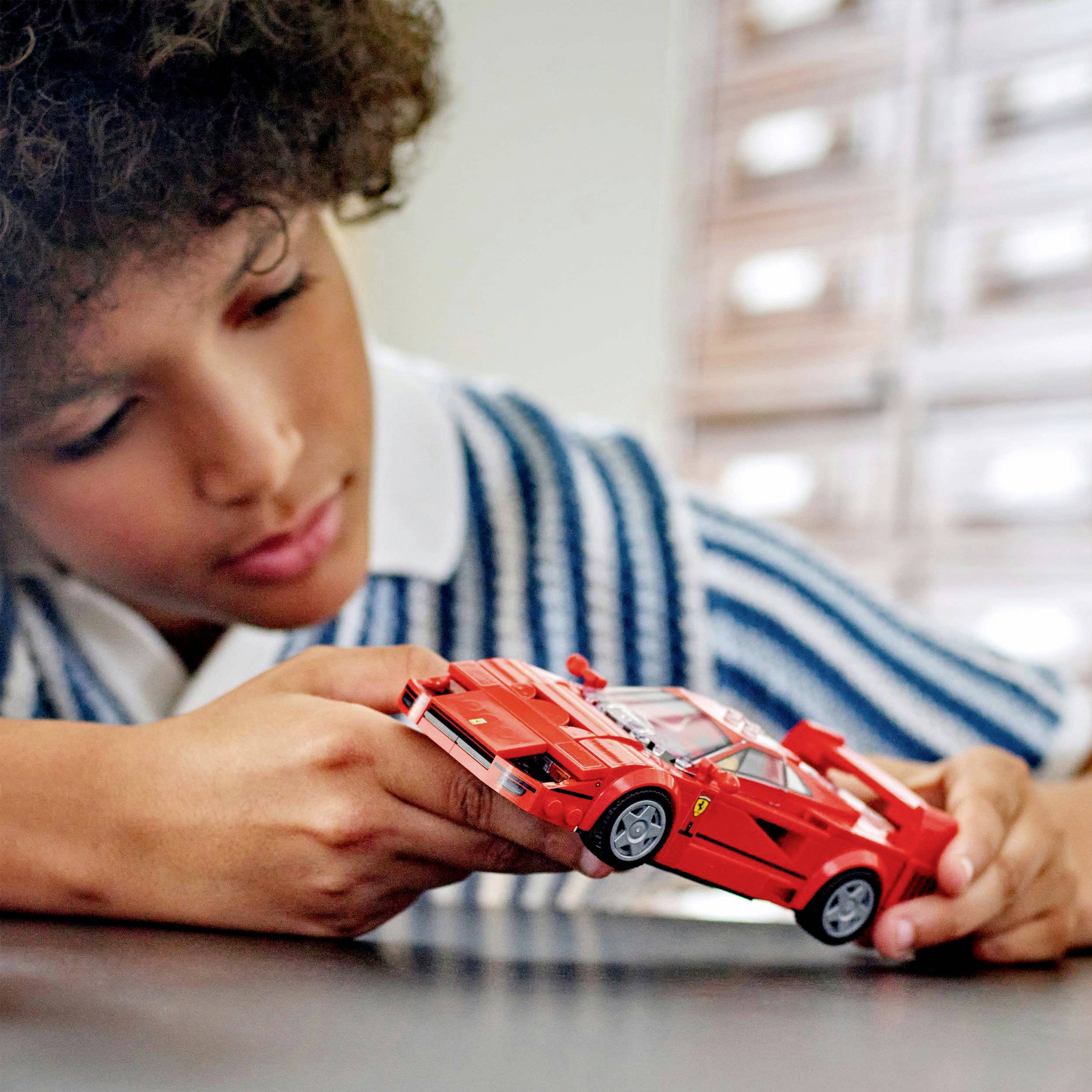 Un enfant joue avec concentration à un petit camion rouge sur une table. Il porte un pull rayé bleu.