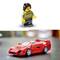 Une figurine LEGO vêtue à la mode Ferrari se tient à côté d'une voiture de jouet LEGO rouge dans le style Ferrari, sur une surface lisse et floue.