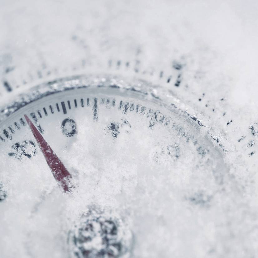 Un thermomètre est recouvert de neige et indique une température légèrement inférieure à zéro degré Celsius.