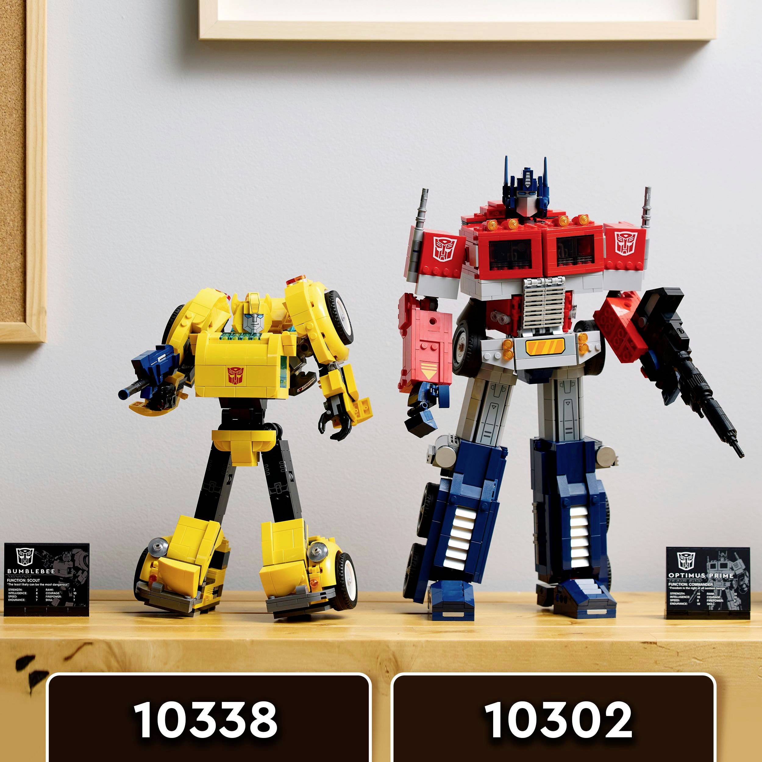 Deux robots Lego, l'un jaune à gauche et l'autre rouge et bleu à droite, sont posés sur une table devant un cadre blanc. En bas se trouvent les numéros 10338 et 10302.