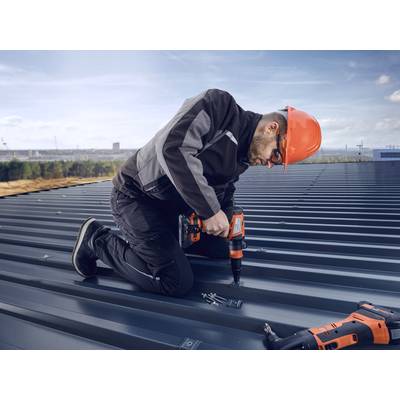 Un ouvrier est agenouillé sur un toit métallique et utilise une visseuse sans fil. Il porte un équipement de protection et un casque orange.