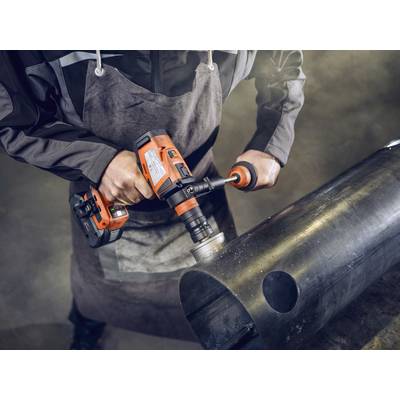 Une personne en tenue de travail utilise une perceuse orange pour travailler un grand tuyau métallique.