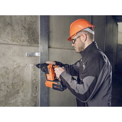 Un ouvrier portant des lunettes de protection et un casque fore un mur en béton avec un marteau-piqueur orange.