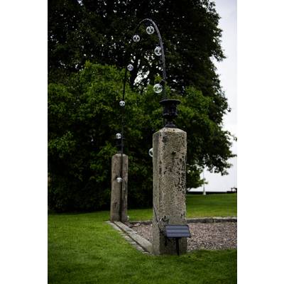Une construction arquée en pierre avec plusieurs boules de verre posées dessus, placée à l'extérieur sur une pelouse verte à côté de grands arbres.