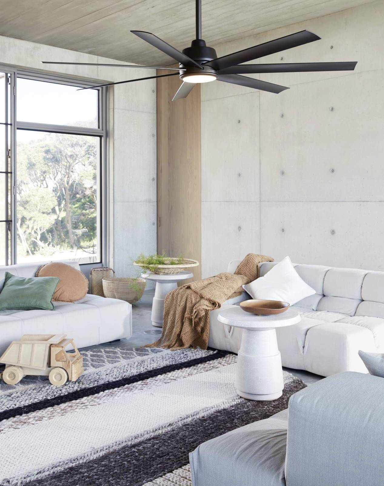 Salon au design moderne : canapés blancs, éléments en bois, grand ventilateur de plafond noir, murs clairs, fenêtre avec vue sur la nature.