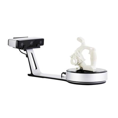 Un scanner 3D capture un objet géométrique blanc sur un plateau tournant. Le scanner dispose d'un support long et d'une caméra rectangulaire.