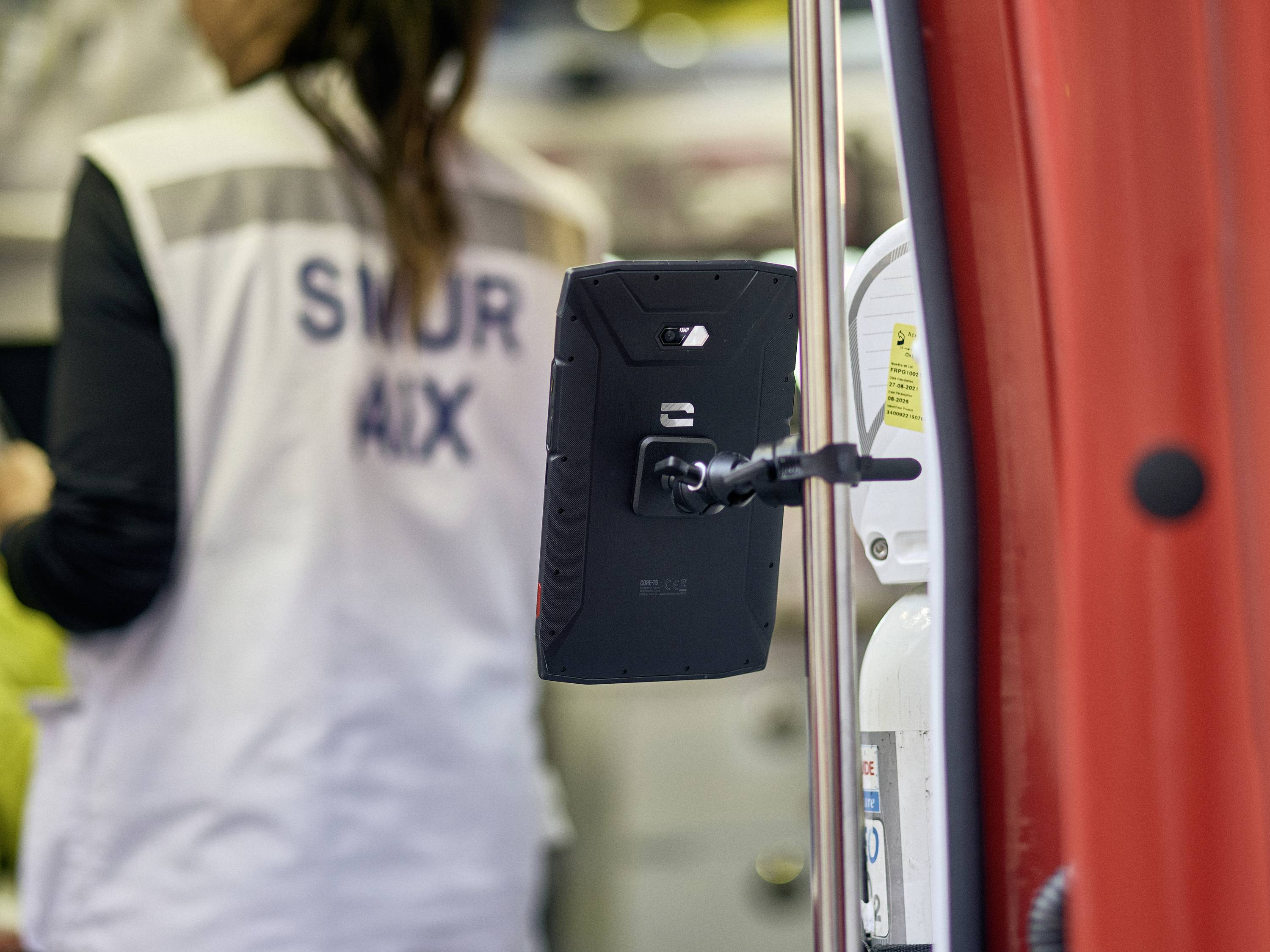 Une personne portant une veste SMUR AIX se tient dans un véhicule de secours. Une tablette est fixée sur un support à l'intérieur du véhicule.