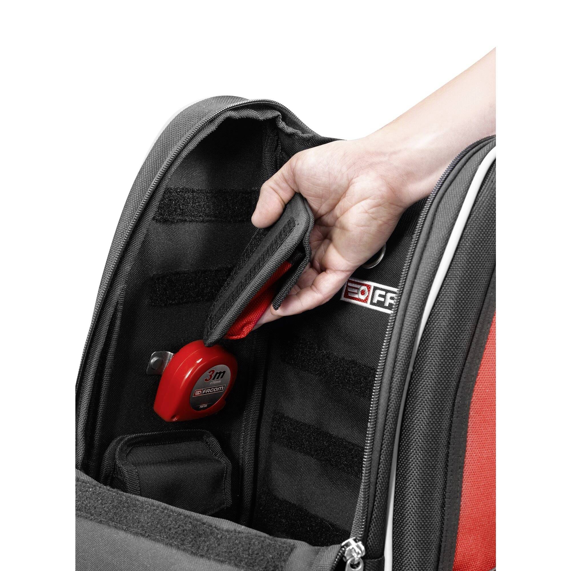 Une personne place un objet rouge portant le logo '3M' dans la poche d'un sac à dos.