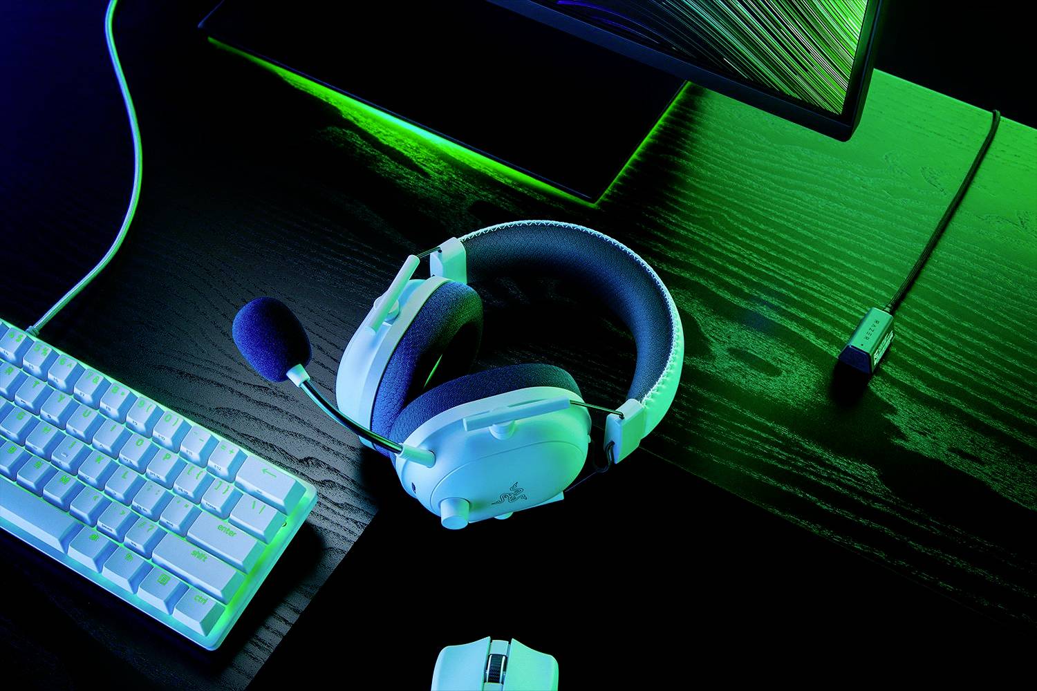 Un casque gaming blanc est posé sur une table en bois sombre à côté d'un clavier et d'une souris d'ordinateur, éclairé par une lumière verte.