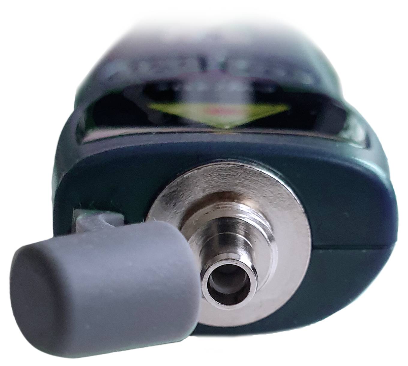 Gros plan d'un petit appareil alimenté par batterie de couleur verte avec une buse métallique et un capuchon gris, isolé sur un fond blanc.