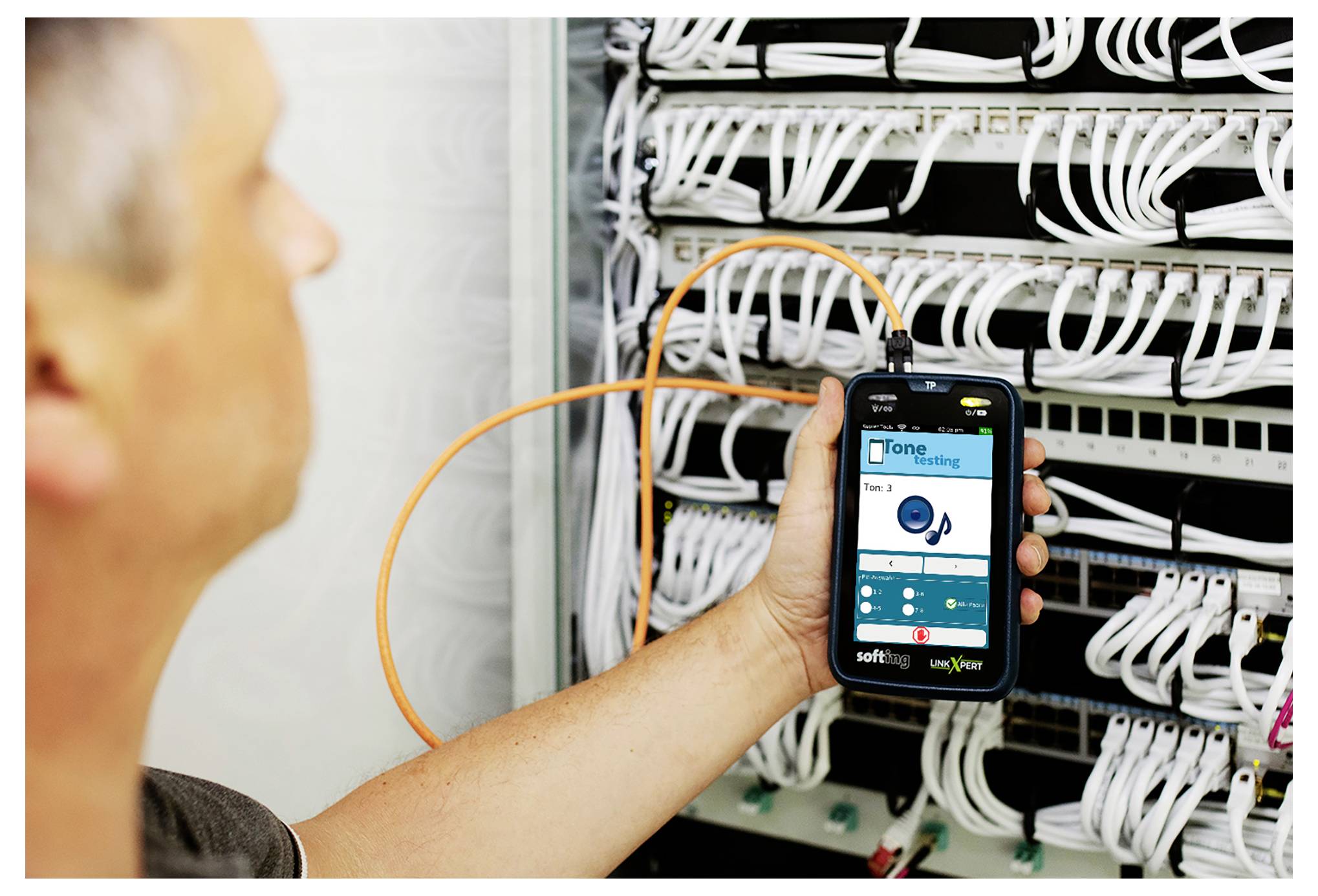 Technicien tenant un smartphone pour inspecter les câbles réseau dans un rack serveur en utilisant une application de surveillance.