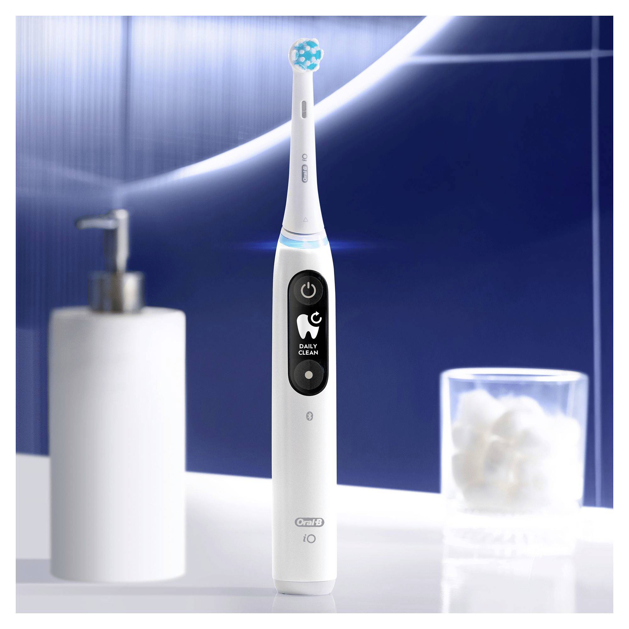 Brosse à dents électrique avec affichage numérique sur un comptoir de salle de bain, à côté d'un distributeur de savon et d'un verre contenant des boules de coton.