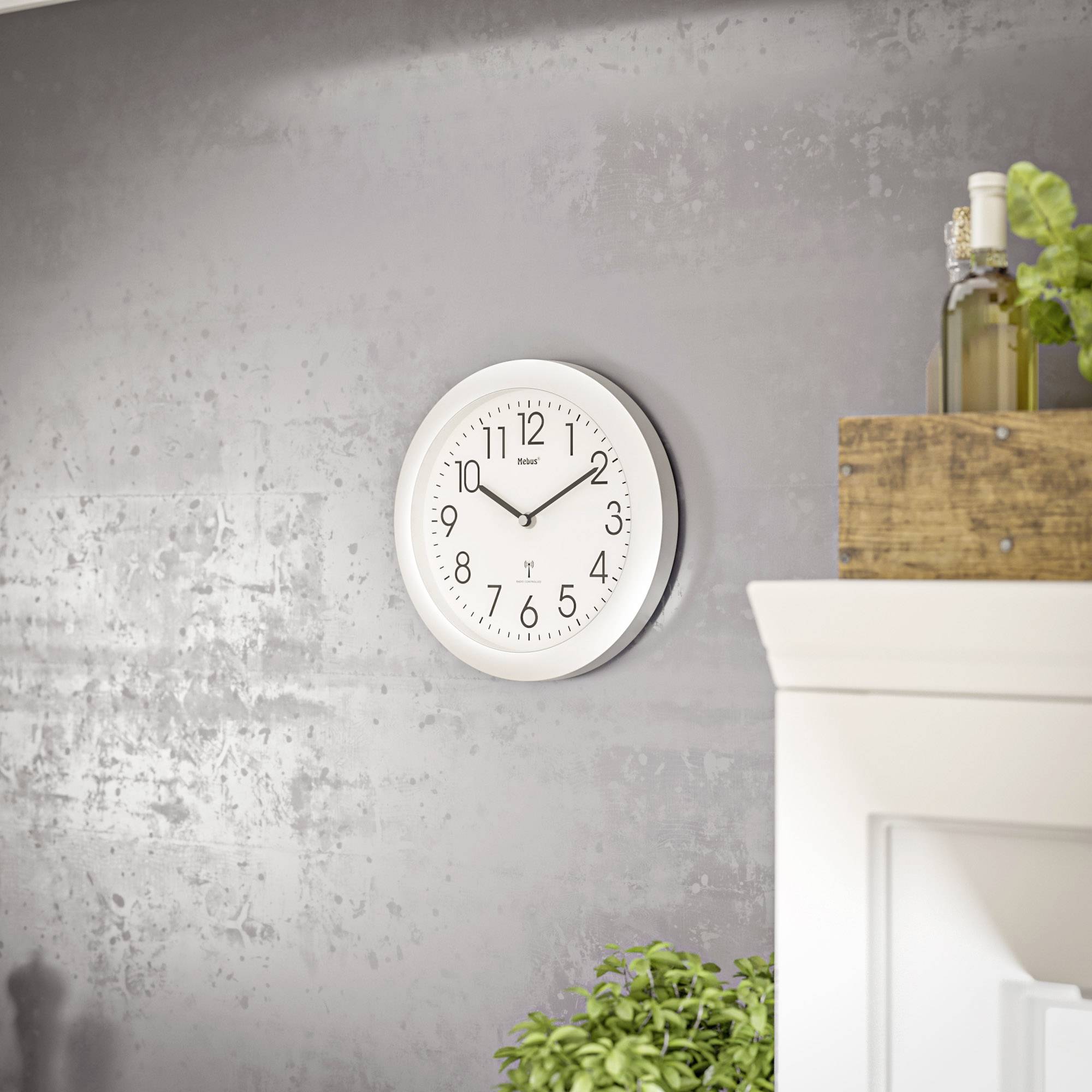 Une horloge murale blanche indique 10h10. À proximité, des caisses en bois contenant des plantes sont posées sur un meuble blanc. L'ambiance est moderne et minimaliste.