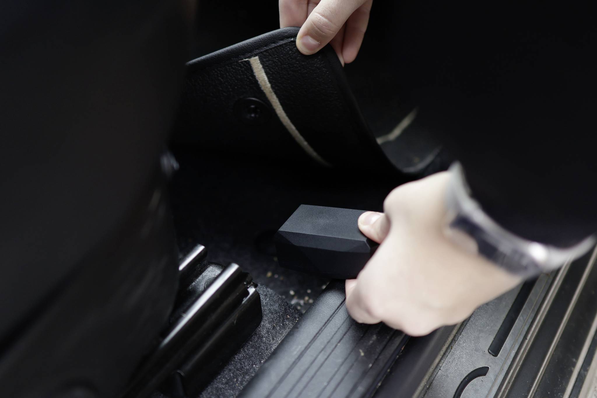Une personne soulève un tapis de sol dans une voiture et découvre un objet caché dessous.