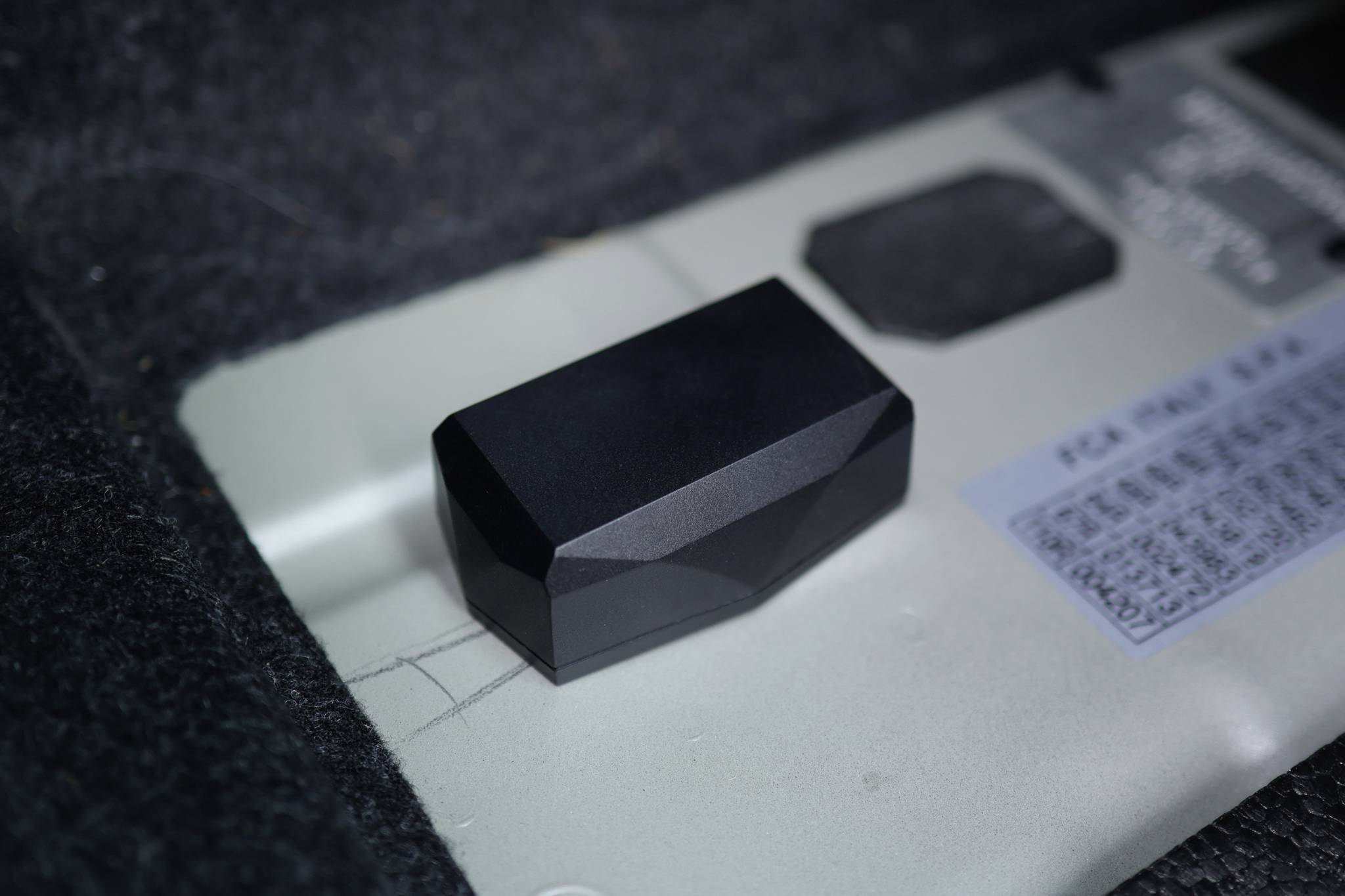 Un objet noir à facettes repose sur une surface grise, à côté d'un panneau dont le texte et les chiffres sont difficiles à déchiffrer.