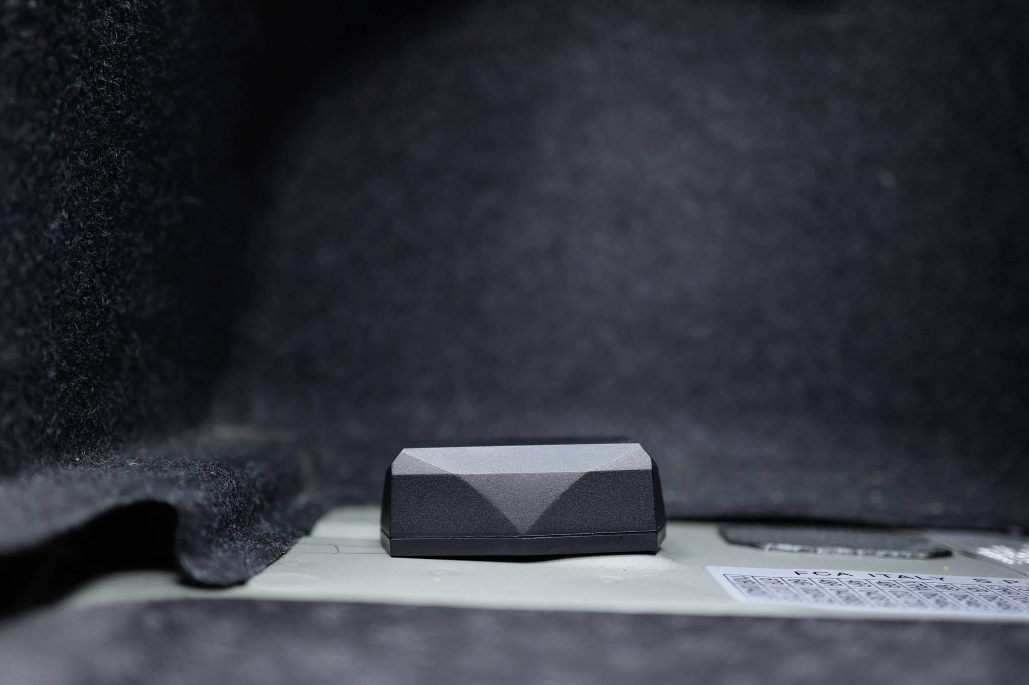 Un bouton noir dans un intérieur capitonné gris, probablement installé dans le coffre d'une voiture.