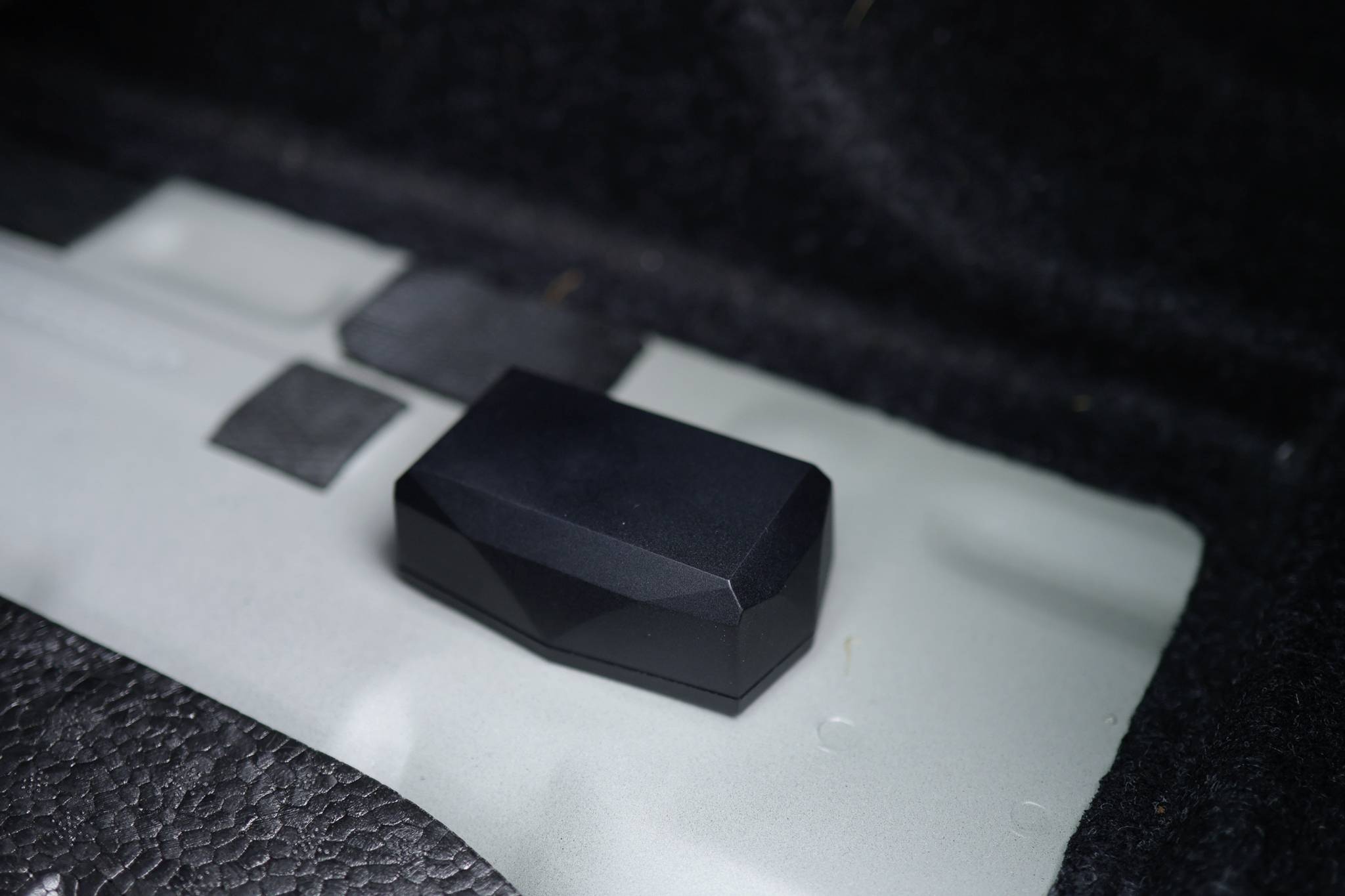 Un objet noir rectangulaire aux coins arrondis repose sur une surface grise, entouré de surfaces noires et grises.