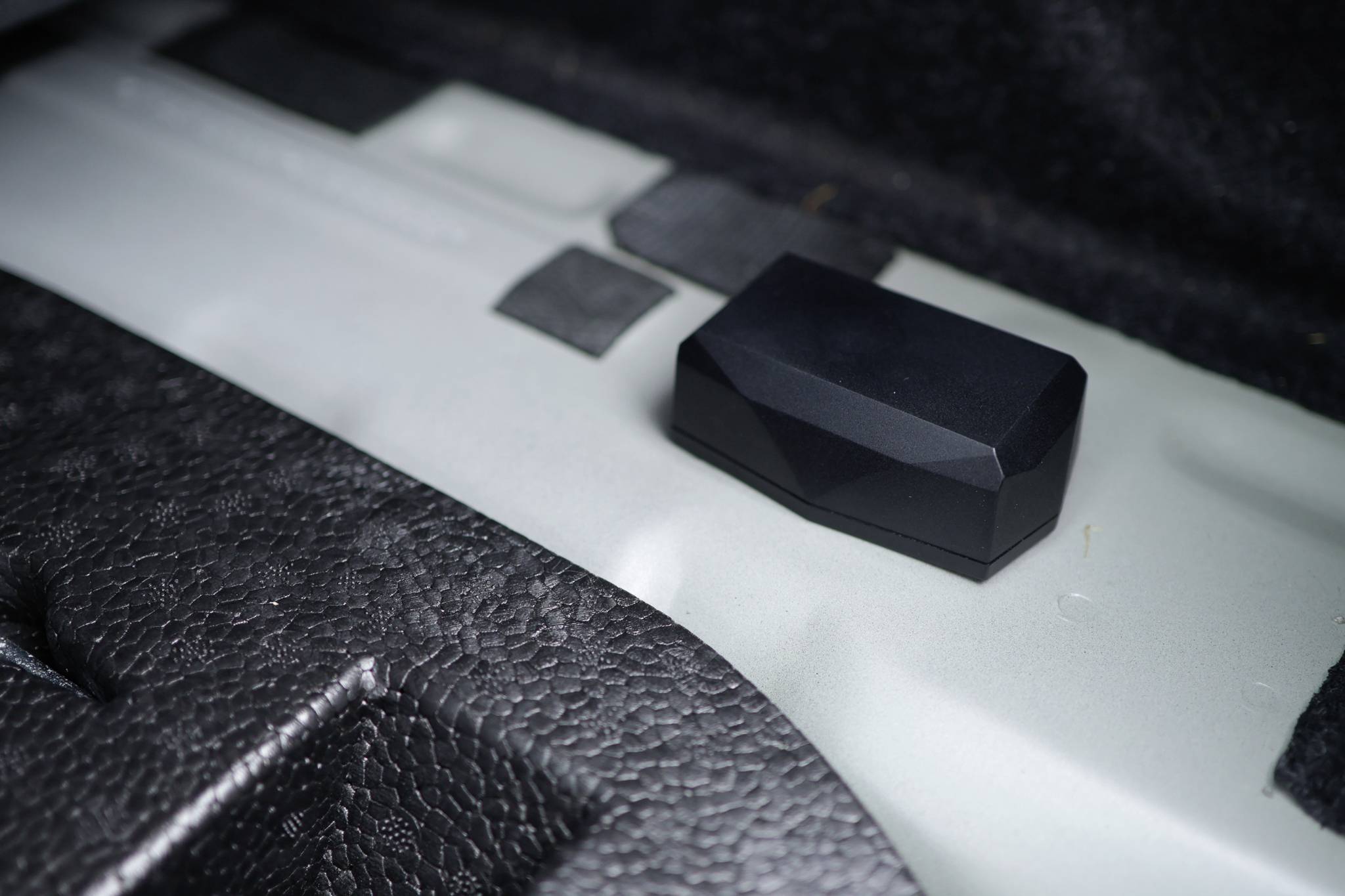 Un objet noir rectangulaire sur un support métallique texturé à l'intérieur d'un véhicule.
