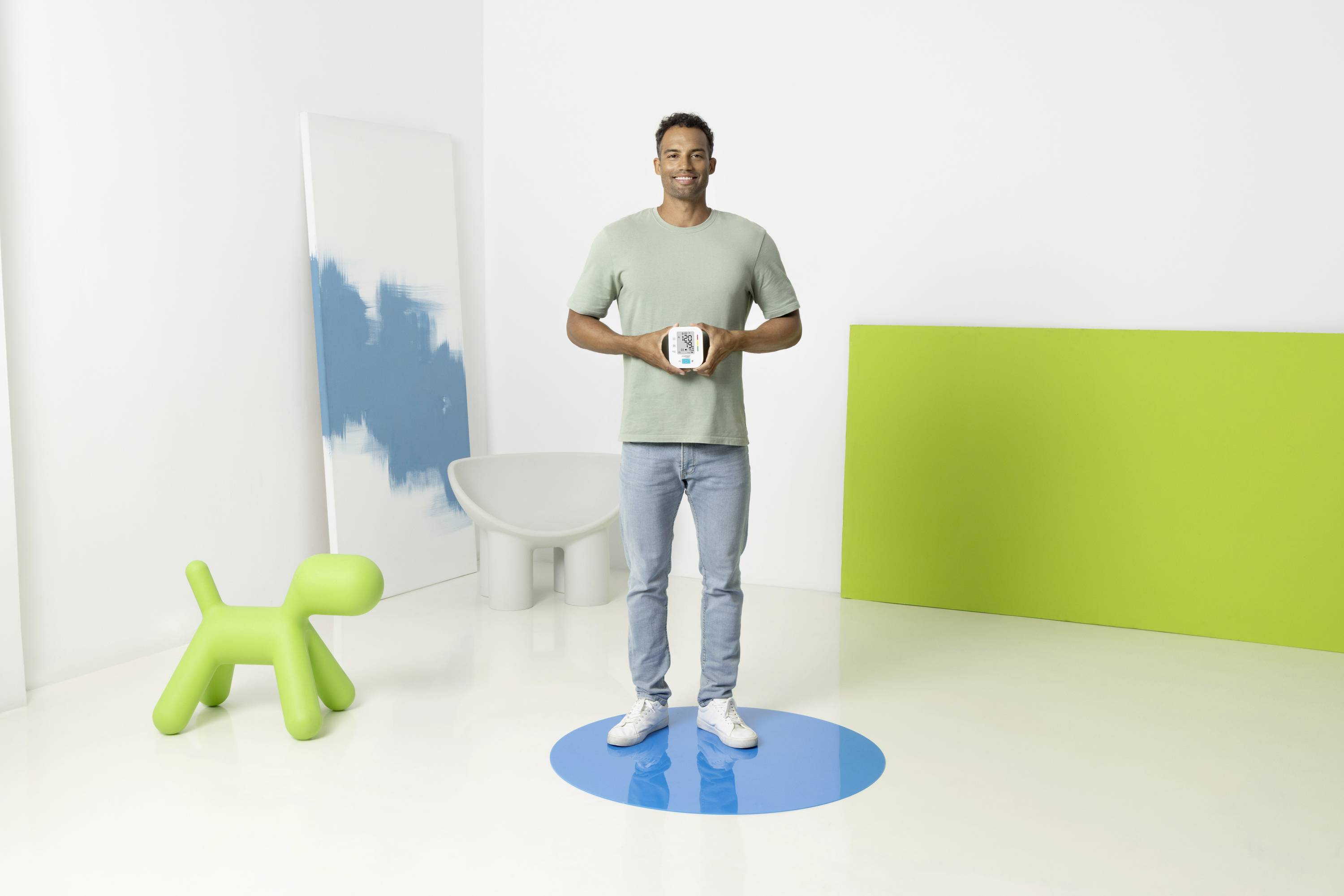 Personne au centre, tenant un appareil. Un chien vert et une œuvre d'art abstraite sont en arrière-plan. L'espace est conçu de manière moderne et lumineuse.