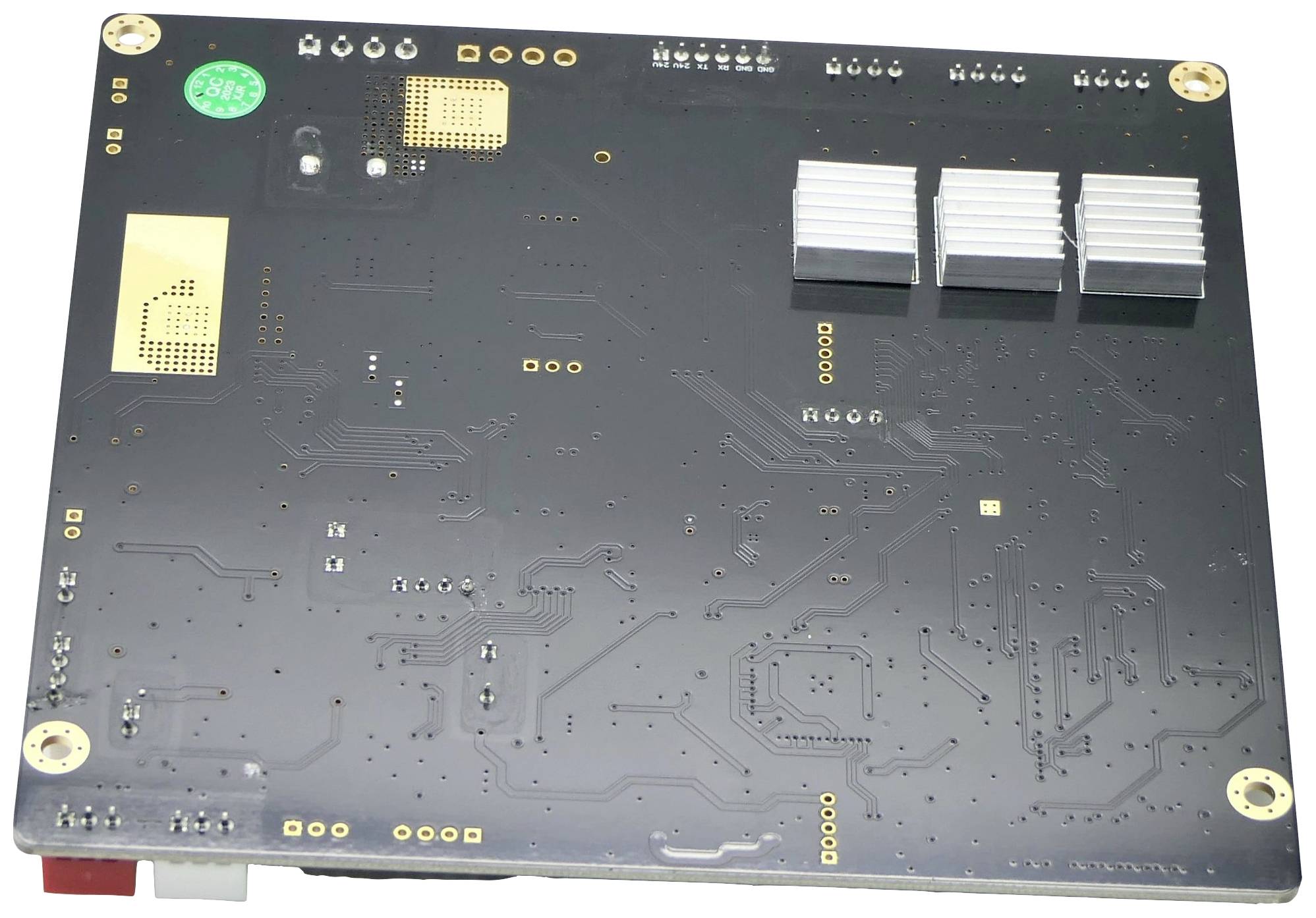 Verso d'une carte mère d'ordinateur avec plusieurs composants électroniques et trois grands dissipateurs thermiques. Aucune connexion visible.