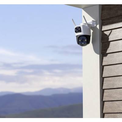 Une caméra de surveillance est montée sur un mur extérieur, orientée vers un paysage de montagnes avec un ciel bleu en arrière-plan.