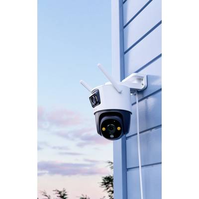 Une caméra de surveillance avec des antennes est montée sur le mur extérieur bleu d'un bâtiment, avec un ciel nuageux en arrière-plan.