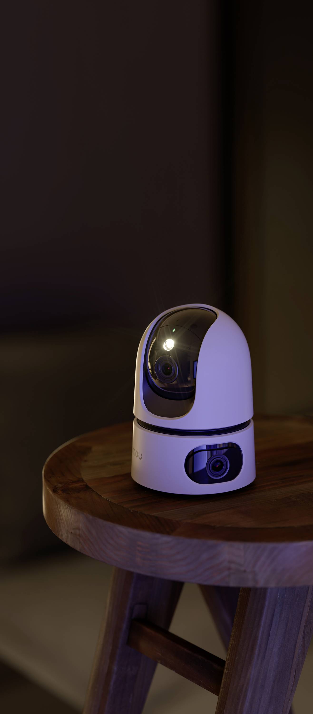 Une caméra de surveillance blanche et pivotante est posée sur une table en bois dans une pièce faiblement éclairée.