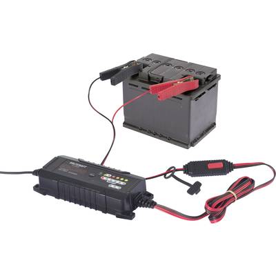 Un chargeur de batterie est connecté à une batterie de voiture. Les bornes sont solidement fixées. Le chargeur affiche le statut de charge.