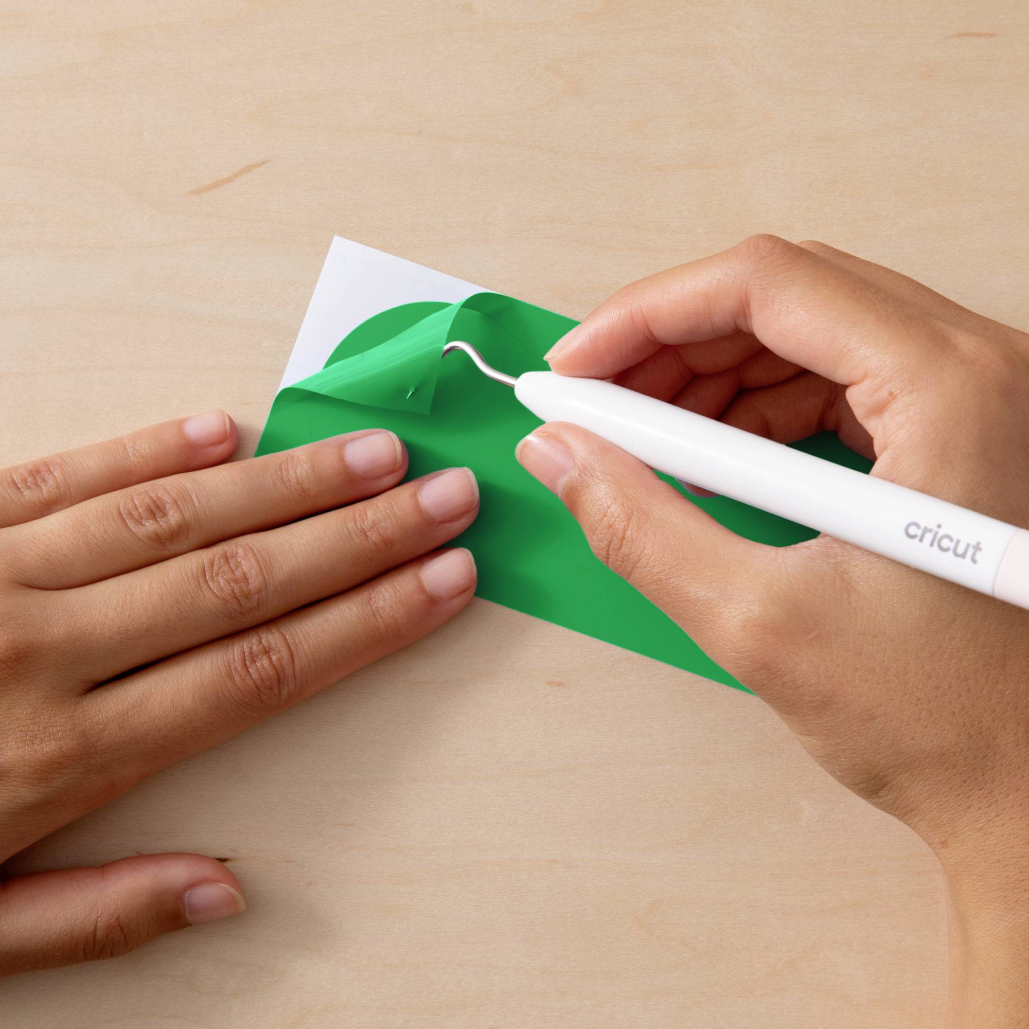 Deux mains retirent du vinyle vert d'une surface adhésive blanche à l'aide d'un outil.