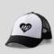 Casquette blanche avec visière noire, sur laquelle se trouve un cœur noir portant les lettres « MB ».