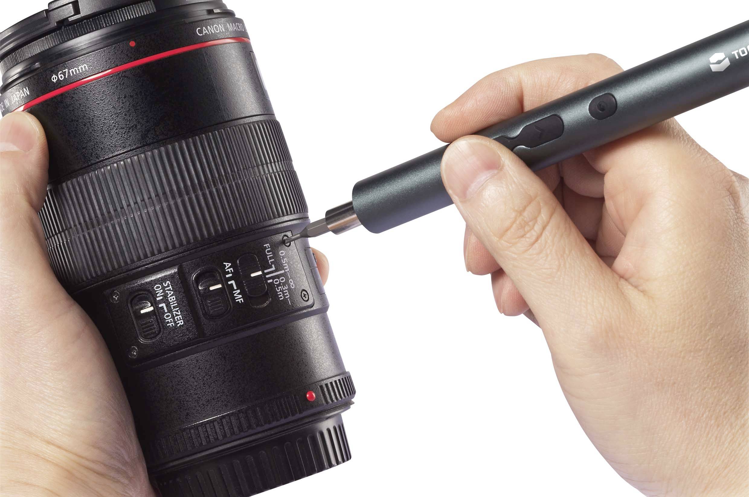 Une personne tient un objectif d'appareil photo dans sa main et utilise un petit outil pour travailler sur les commutateurs de l'objectif.