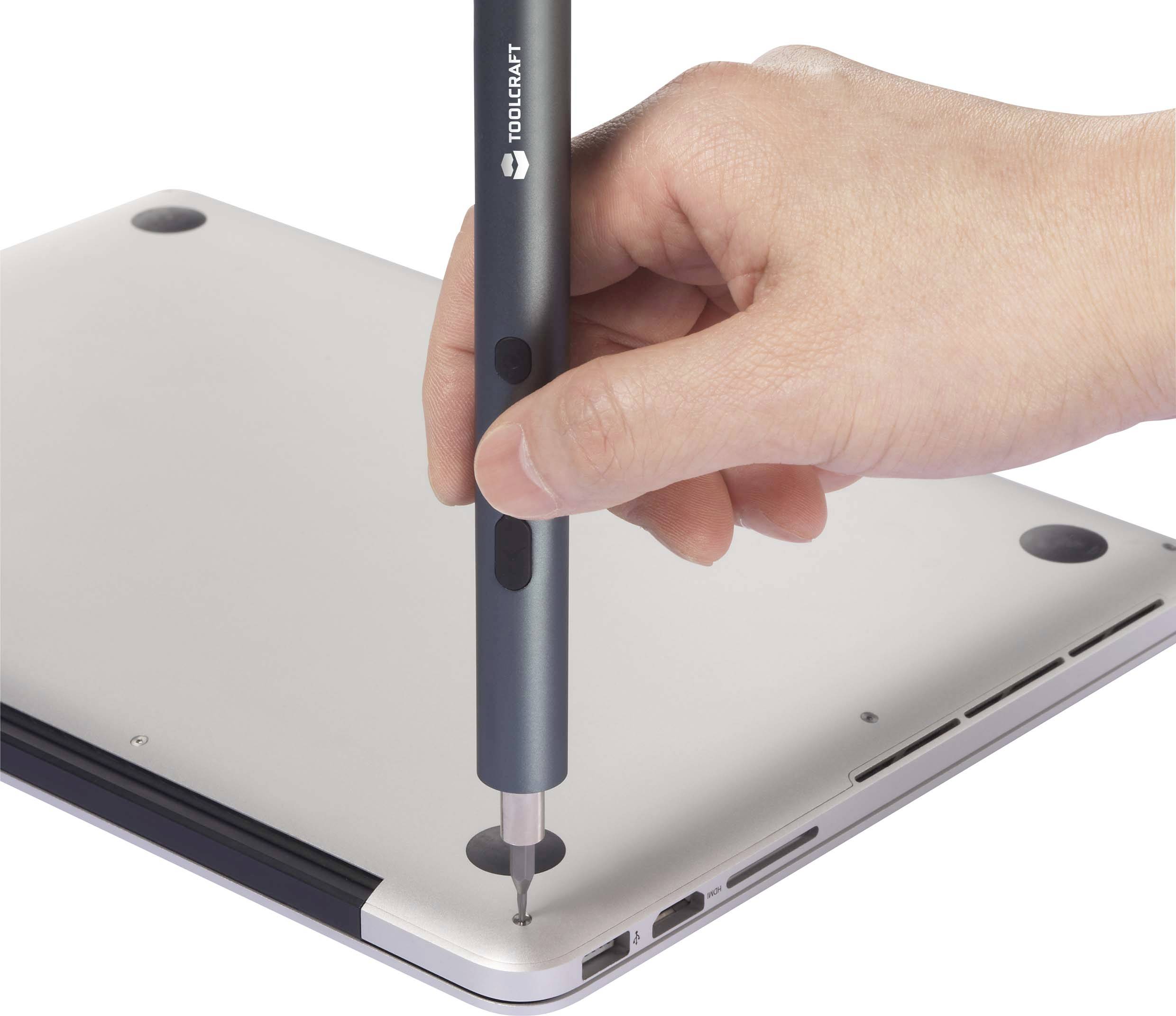 Une main tient un tournevis qui est utilisé pour retirer une vis sous un ordinateur portable.