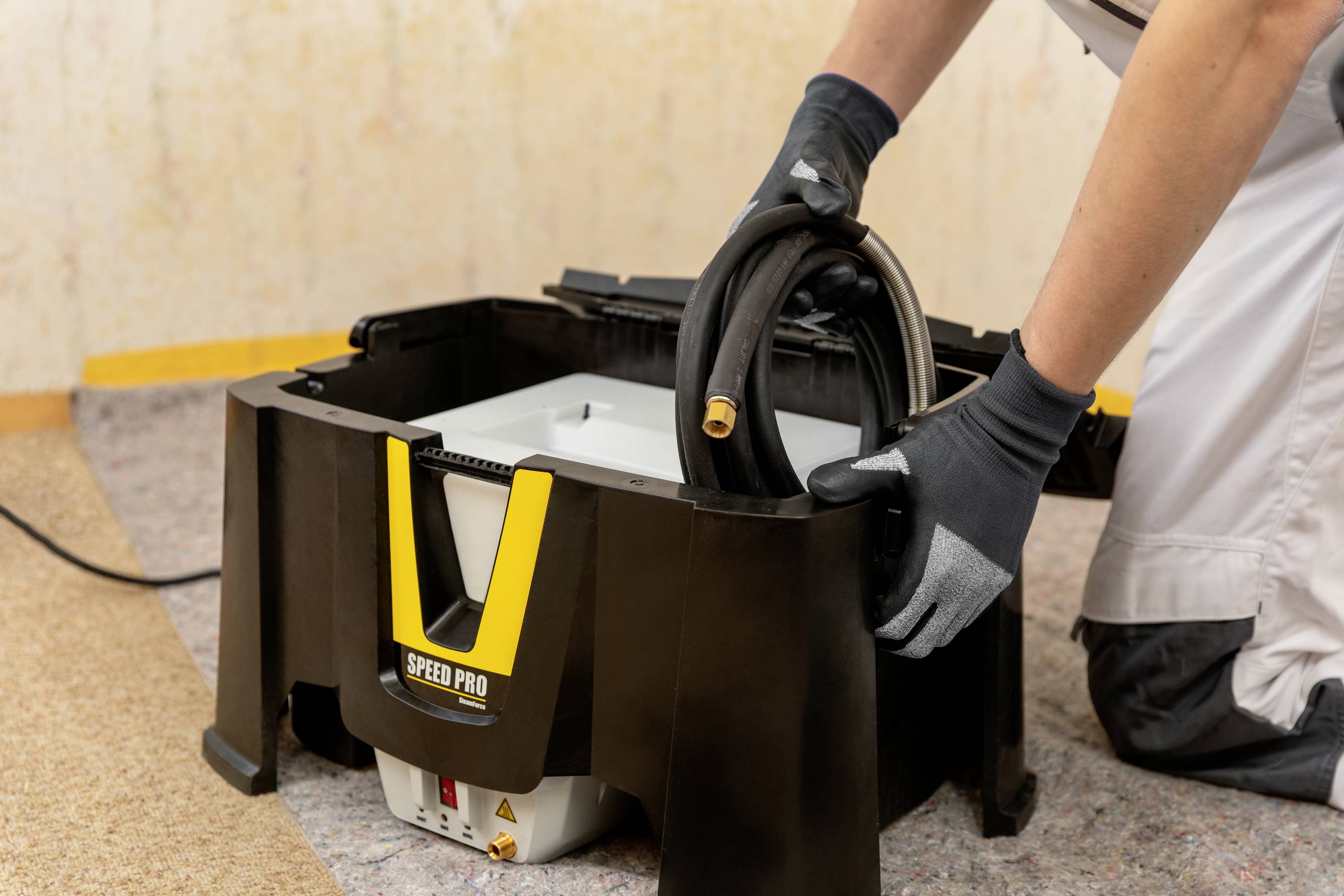 Une personne enroule un câble noir qui sort d'un appareil ressemblant à un aspirateur de chantier ou industriel.