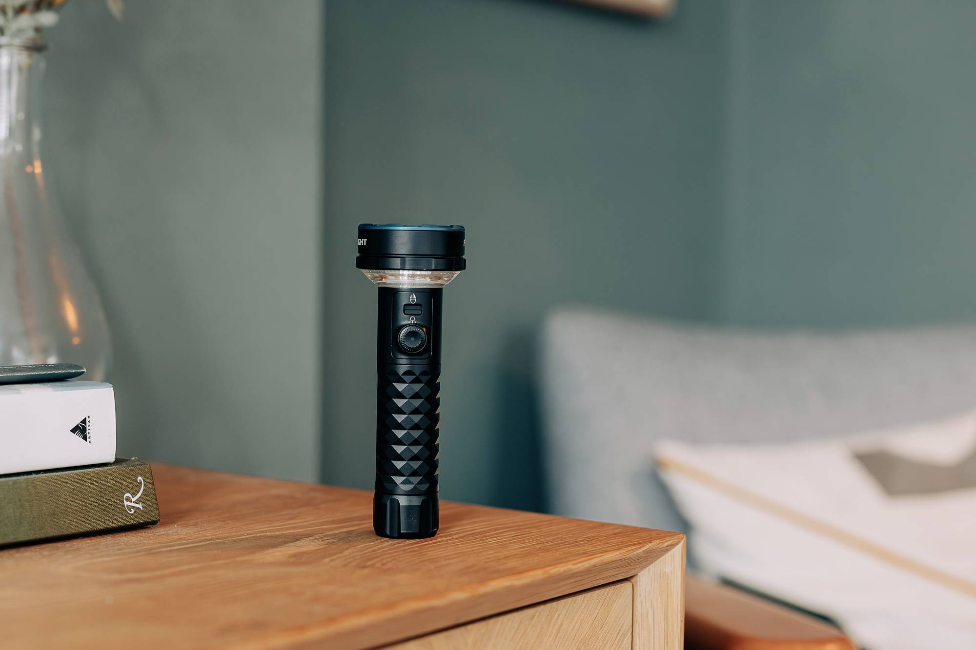 Une lampe de poche noire est posée sur une table en bois à côté d'une pile de livres, dans une pièce décorée avec goût.