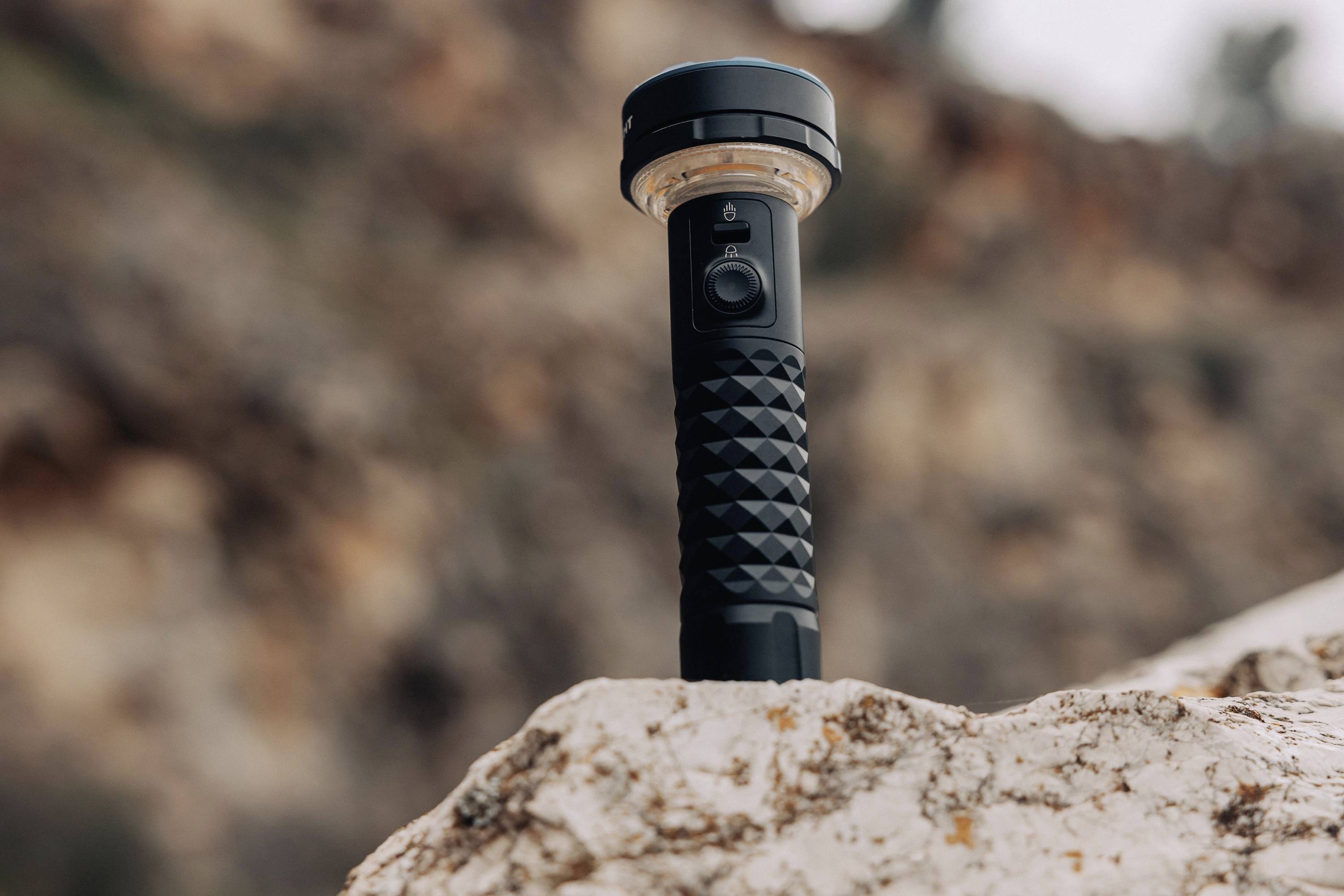Une lampe de poche noire est posée sur un rocher devant un arrière-plan rocheux flou.