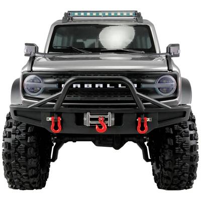 Véhicule tout-terrain vu de face en gros plan avec des pneus robustes, un pare-chocs et un treuil. Une barre LED montée sur le toit est visible en arrière-plan.
