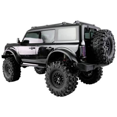 Grand véhicule tout-terrain noir avec une garde au sol élevée, de grandes roues tout-terrain et deux roues de secours à l'arrière, vue latérale.