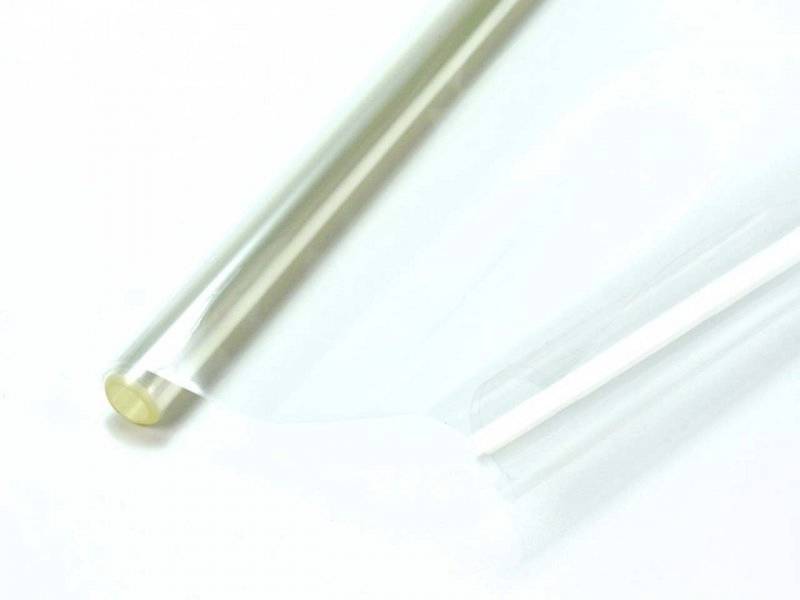 Feuille de plastique transparente sur un fond blanc, légèrement enroulée à une extrémité, reflétant une faible lumière.