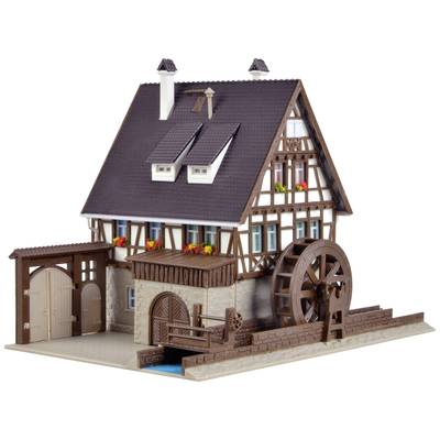 Une maison à colombages avec une roue à eau, de petites fenêtres, des jardinières fleuries, une cheminée et des bâtiments annexes. Elle est construite sur un soubassement en pierre.