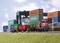 Un train miniature avec des wagons porte-conteneurs circule à travers un port de conteneurs miniature. Plusieurs figurines interagissent avec l'environnement.
