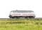 Un modèle d'un train Intercity gris argenté sur une section de voie ferrée, entouré d'herbe verte.