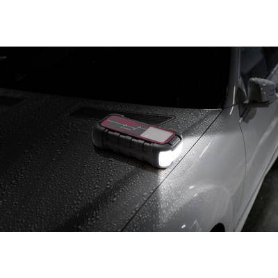 Une batterie externe noire avec lampe torche est posée sur le capot d'une voiture mouillée.