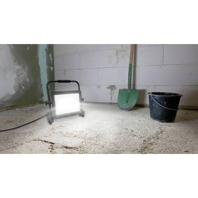 Un chantier avec une lampe de travail illuminée posée sur le sol, une pelle et un seau à côté d'un mur inachevé.