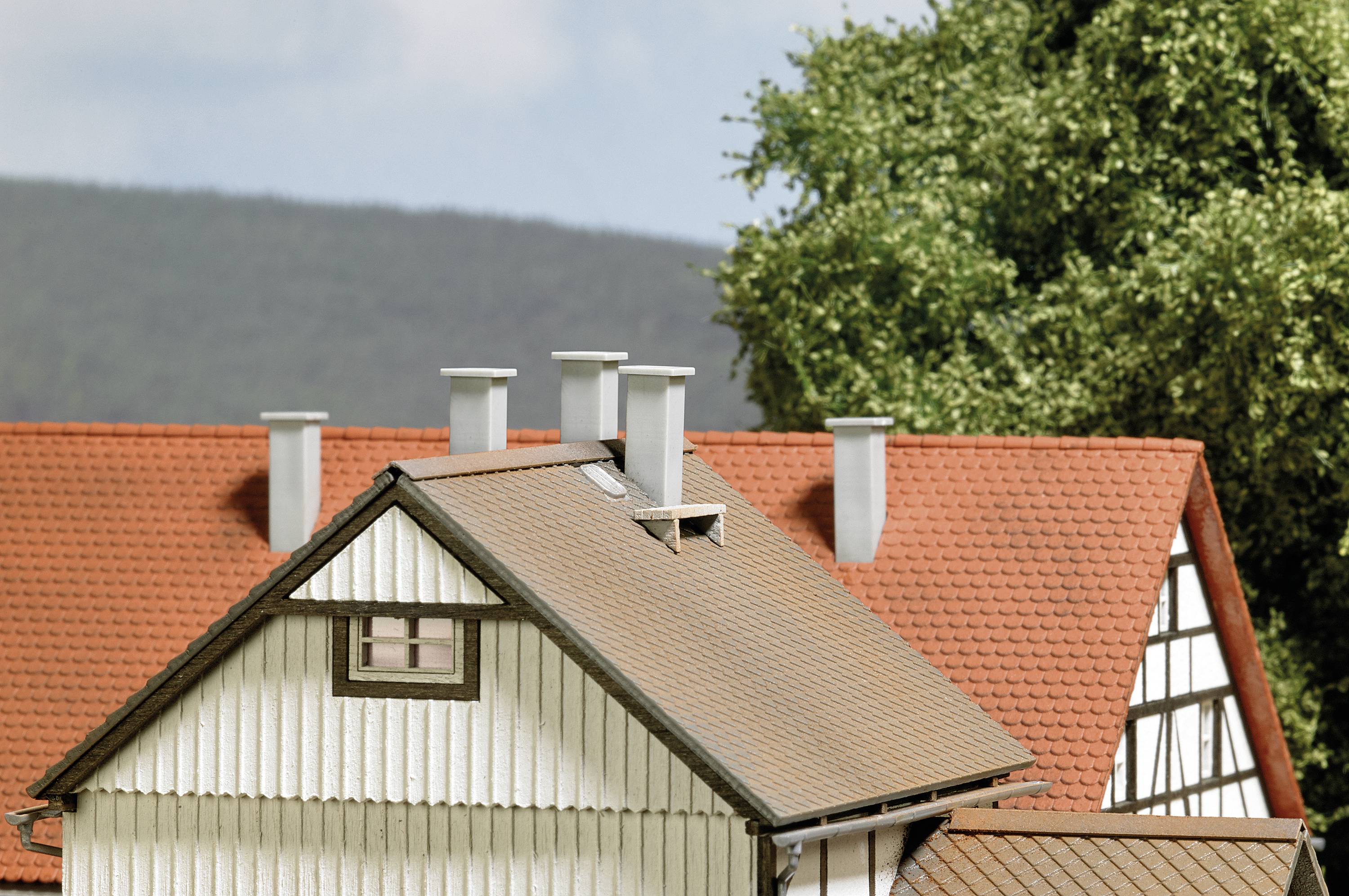 Une maison à colombages traditionnelle avec un toit en tuiles rouges et plusieurs cheminées, entourée de paysages verdoyants et d'arbres.