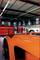 Dans un atelier automobile, une voiture d'un orange éclatant se trouve au premier plan, entourée d'armoires à outils et d'autres véhicules.
