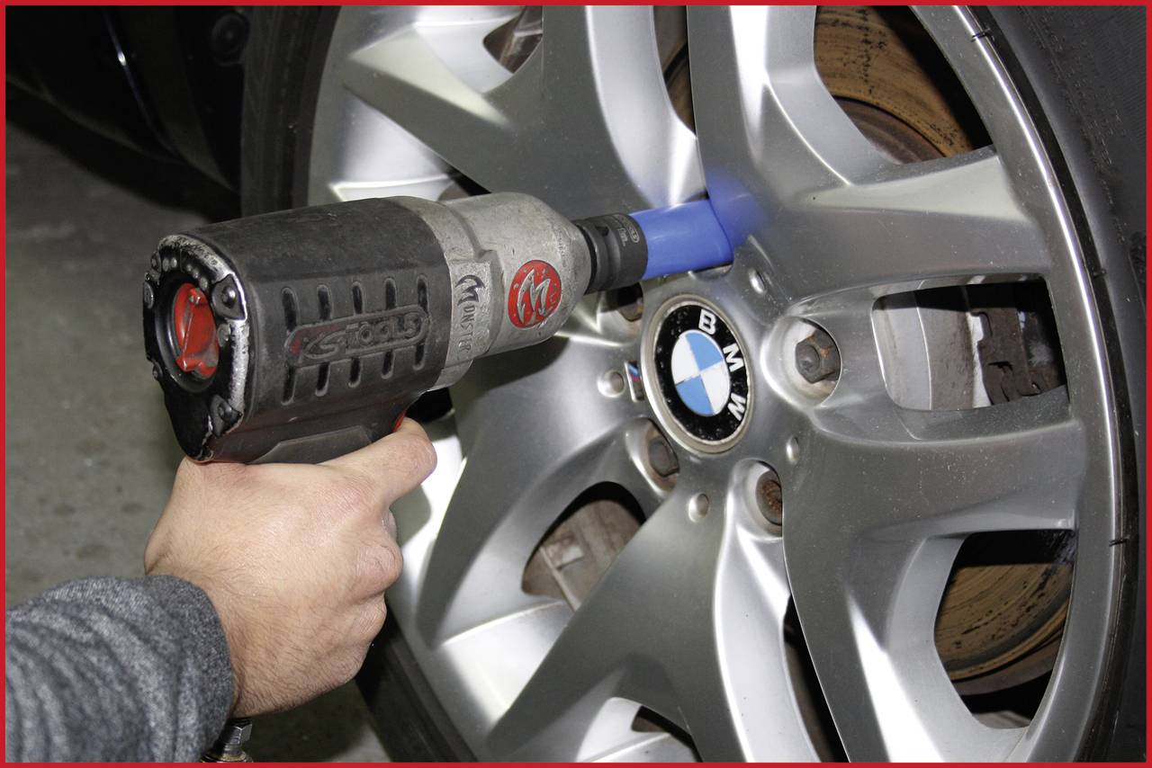 'Une main utilise une visseuse à percussion pour serrer une vis sur un pneu de BMW.'