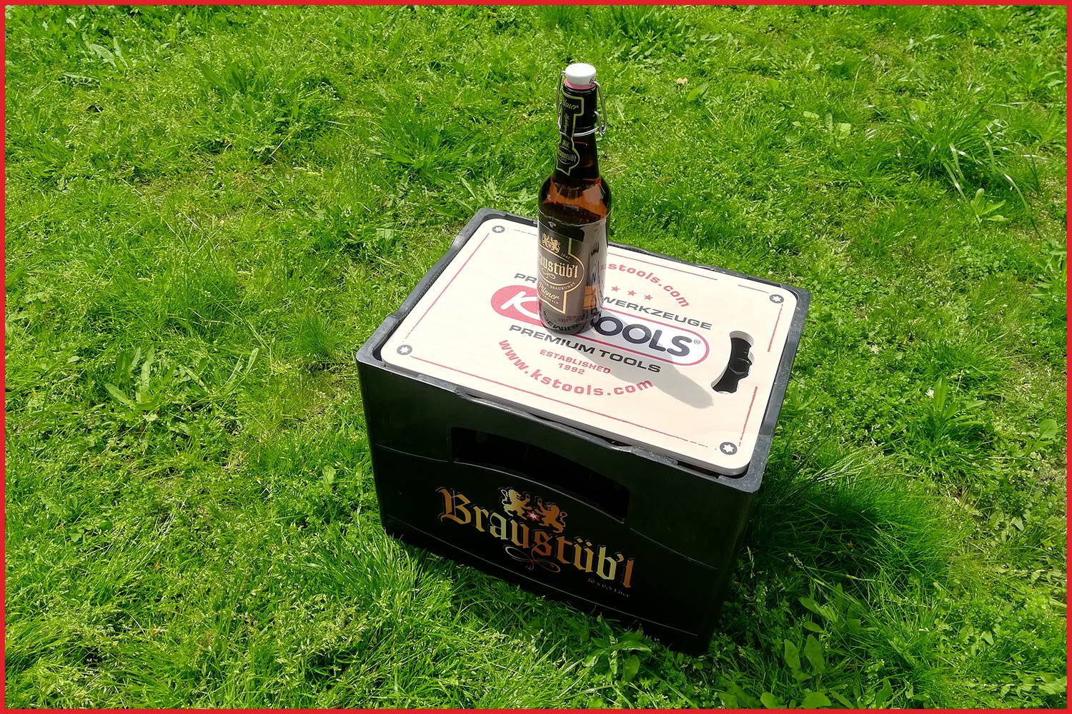 Une caisse de bière fermée de la marque 'Braystädtl' est posée sur un pré. Une seule bouteille de bière est placée sur le dessus de la caisse.