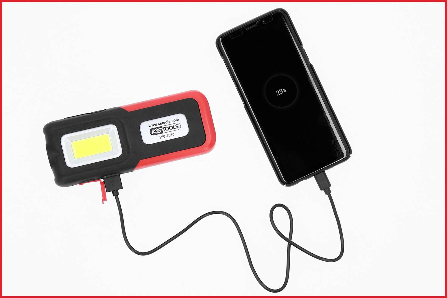 Une lampe portable avec port USB charge un smartphone. Le téléphone affiche '23%' sur l'écran comme niveau de batterie.
